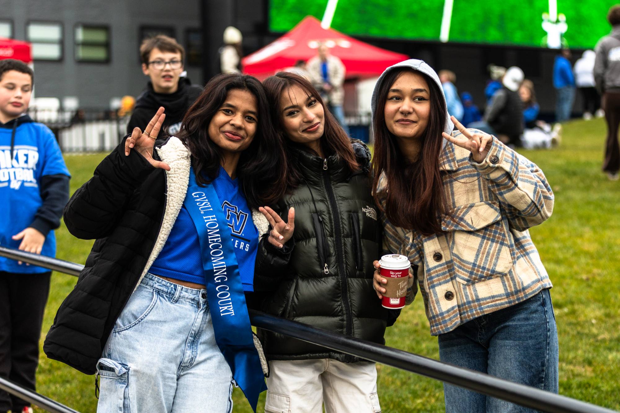 three girls hold up the anchor up sign while at a football game